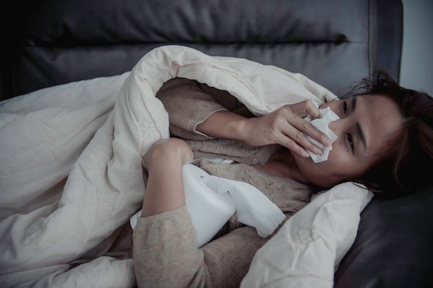 アジアの病気の女性がソファに座って家にいる女性は気分が悪くなり、横になりたいと思った