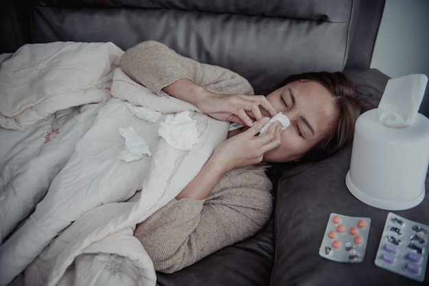 アジアの病気の女性がソファに座って家にいる女性は気分が悪くなり、横になりたいと思った