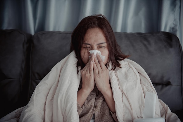 Asian sick woman sit on the sofa stay at homeThe woman felt bad wanted to lie down and resthigh fever