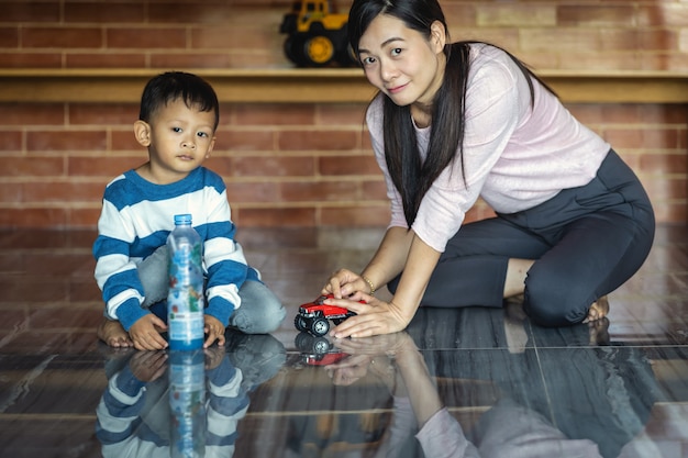 現代の家に住んでいるときに息子とアジアのシングルママは一緒に車のおもちゃで遊んでいます。