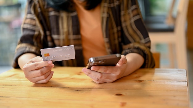 An Asian sitting in the coffee shop using her smartphone and credit card to pay online bills