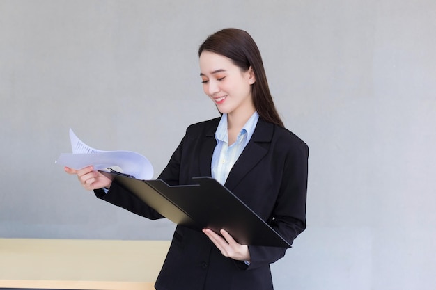 Asian smart business female manager is smiling confidently while she holds opens document clipboard