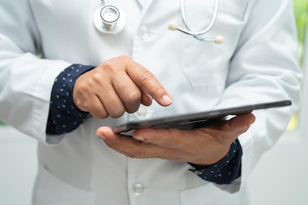 Asian smart man doctor holding digital tablet technology to search knowledge solve treatment for patient in hospital