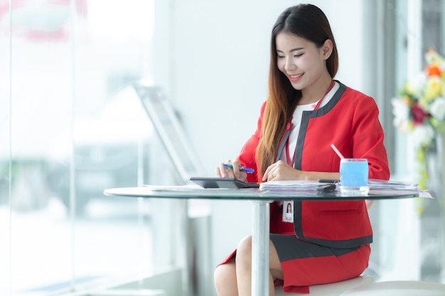 Asian smiling businesswoman in suit talking on phone using tablet sitting at office workpl