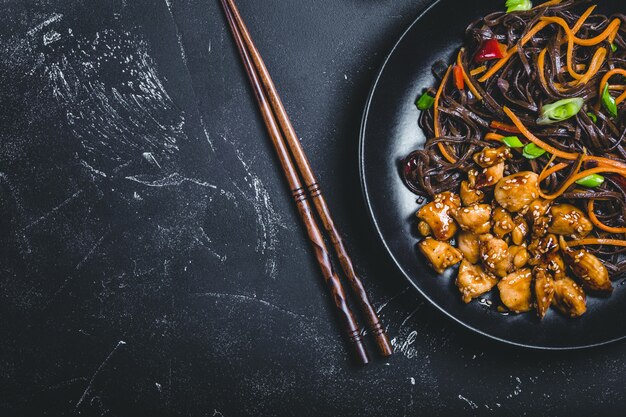 Foto tagliatelle asiatiche di soba, pollo, verdure, sfondo scuro. spazio per il testo.