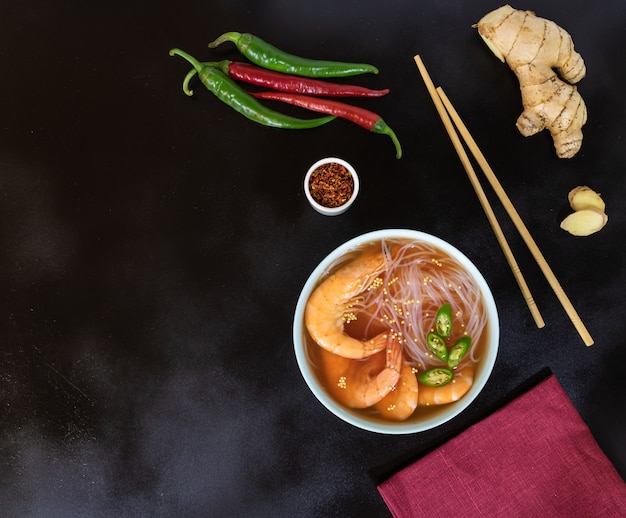 Asian soup with shrimps, rice noodles, ginger and hot pepper on black 