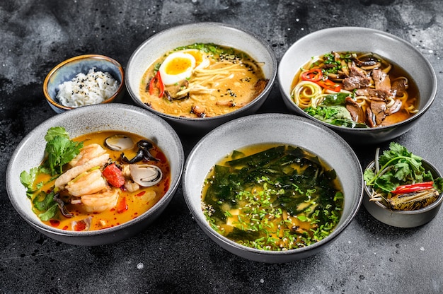 Asian soups, Miso, Ramen, Tom Yam, Pho Bo. Black background. Top view