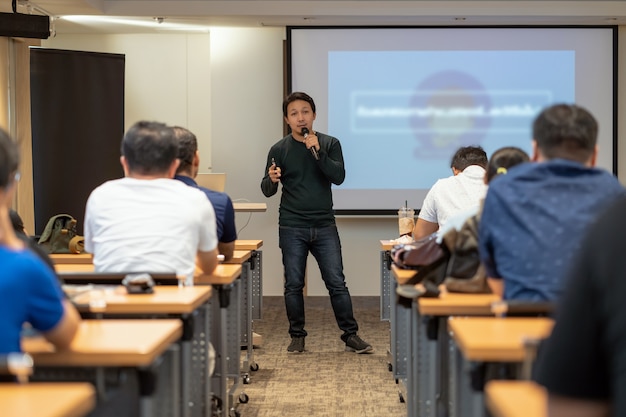 Asian Speaker with casual suit on the stage in front of the room with low light