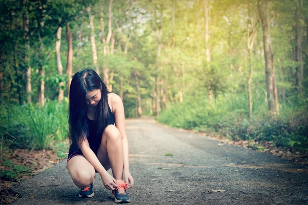 Asian sport girl sitting and tie her shoelaces before jogging in the park