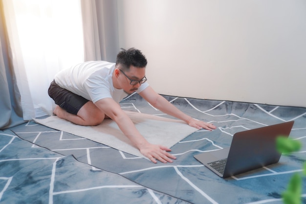 Foto uomo sportivo asiatico che fa yoga e fitness a casa usando il laptopvista laterale dell'uomo che pratica yoga in