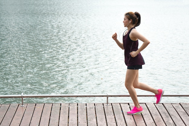 Asian sport woman jogging on lake rim in park 