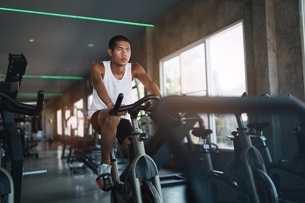 Азиатский спортсмен, тренирующийся на велосипеде в тренажерном зале, решимость кардио похудеть делает ее здоровой концепцией фитнес-спорта для велотренажера