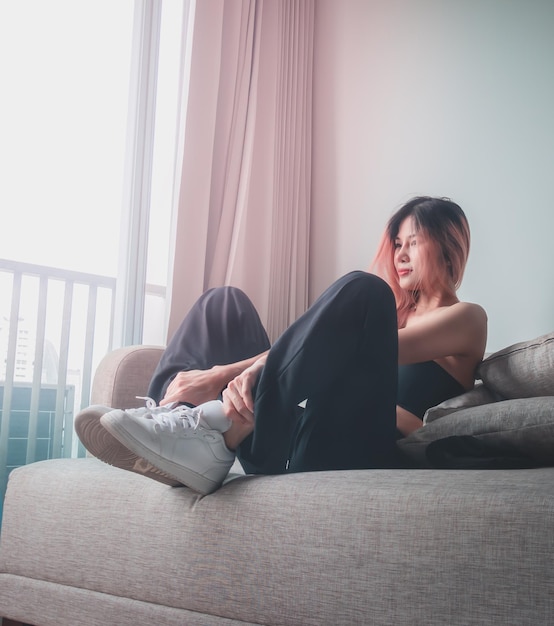 Foto asian sporty fashion model girl poseert met witte sneakers schoenen op sofa in een appartement voor coole street sport fashion