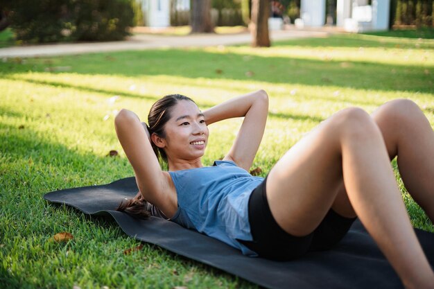 Asian sporty girl doing abdominal crunches on a mat on the grass in the park