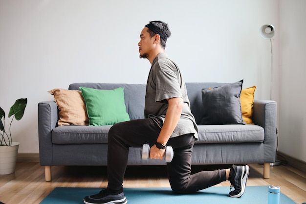 Asian sporty man doing exercise with dumbbell on yoga mat at home