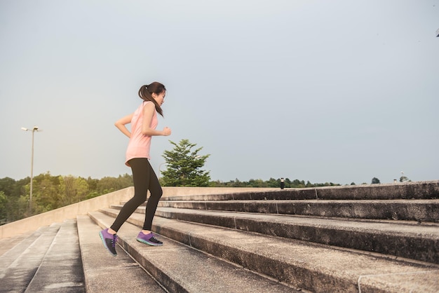 Asian sporty woman running outdoors in park from back angleThai female run up stair in the eveningYoung lady heathy lifestyle