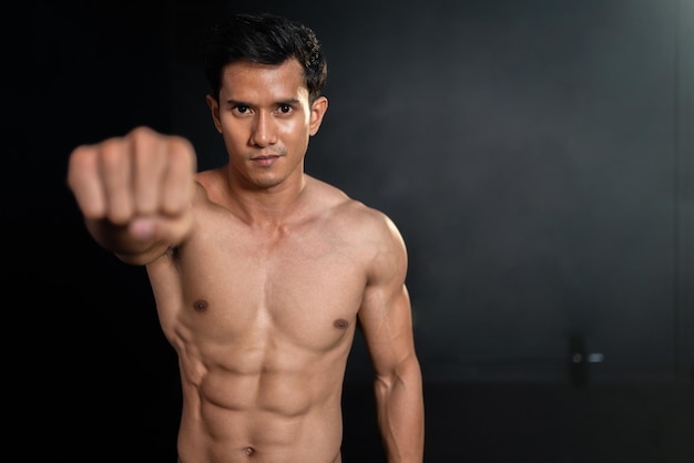 Asian strong muscular man clench fist showing six pack in fitness gym