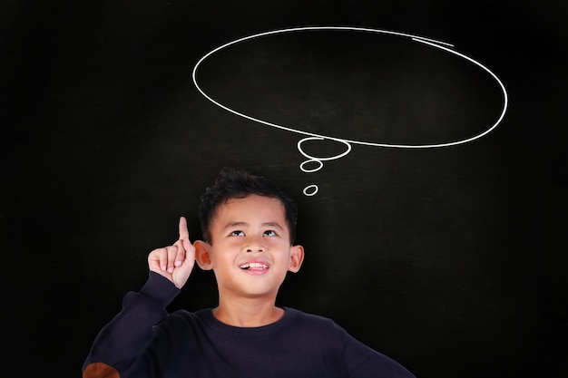 Photo asian student boy smile pointing finger up idea gesture over blackboard empty dreaming speech bubble