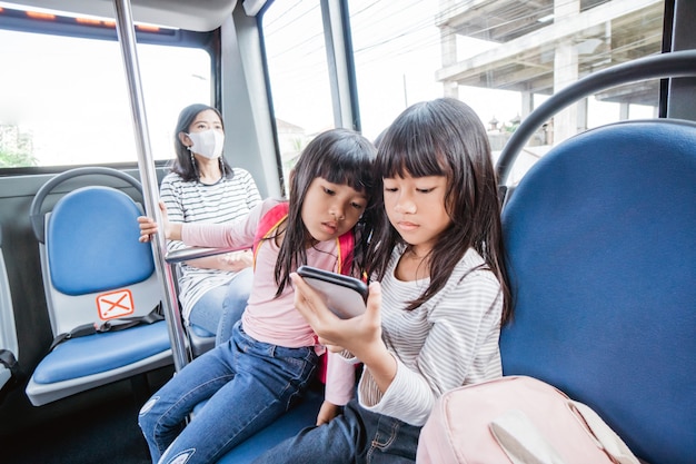 学校に行く途中で一緒に公共バスに乗ってスマートフォンを使用してアジアの学生の女の子