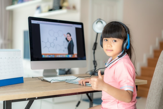 Asian  student girl video conference e-learning with teacher on computer and thumb up in living room