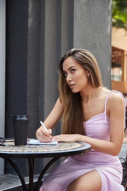 Asian student girl with cup of coffee outside of cafe studying writing notes