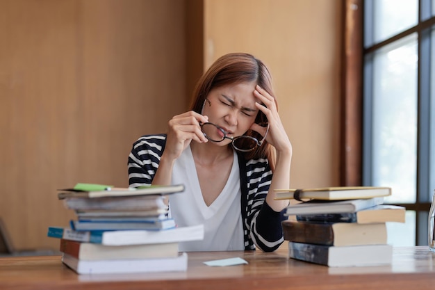 大学図書館で最終試験を読んでいるアジアの学生手で座っている頭痛