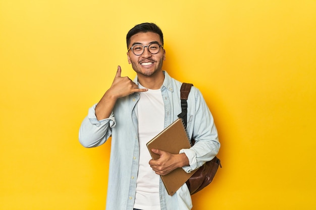 Asian student with backpack and notebook showing a mobile phone call gesture with fingers