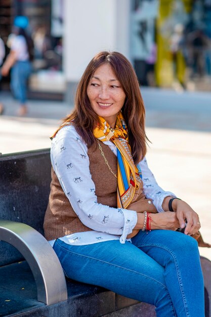 Азиатская стильная женщина читает поздравительную открытку, сидя на скамейке в городе