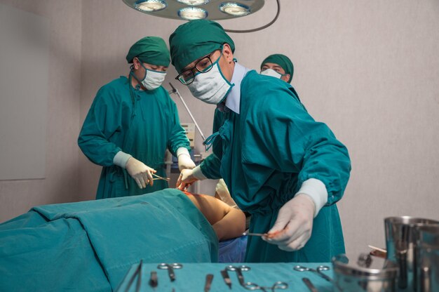 심각한 부상을 입은 환자를 수술하고 병원의 수술실에서 의료 장비를 집는 아시아 외과 의사 팀