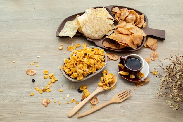 Spuntini dolci e salati asiatici, gustosi cornflakes misti, banana fritta e taro fritto, noce, uva e caramello su fondo di legno luce naturale. snack dolci con una tazza di tè e copia spazio