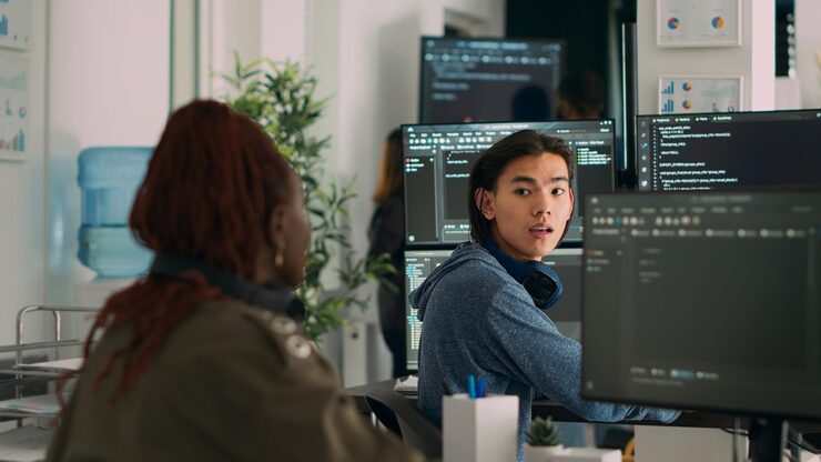 Photo asian system engineer asking coder for help with html code, pointing at database script on terminal window. team of diverse developers working on app developing program in data room.