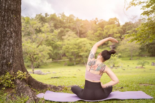 Asian tattoo young woman doing yoga in the park