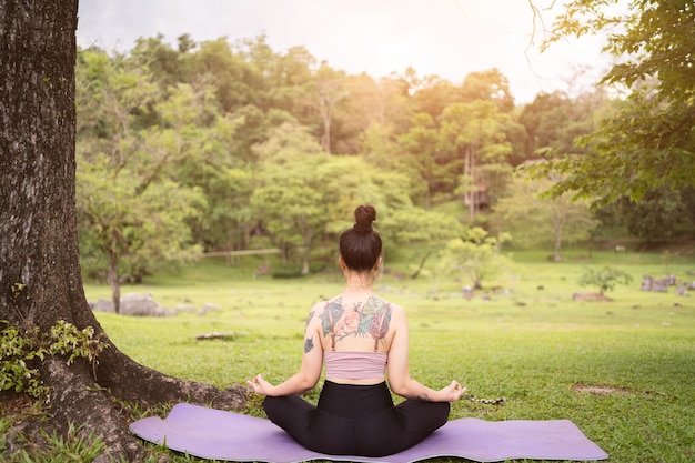 Asian tattoo young woman doing yoga in the park