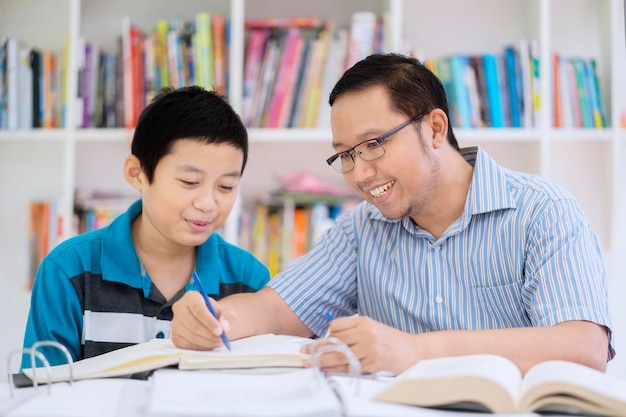 Asian teacher helping his student to read a book