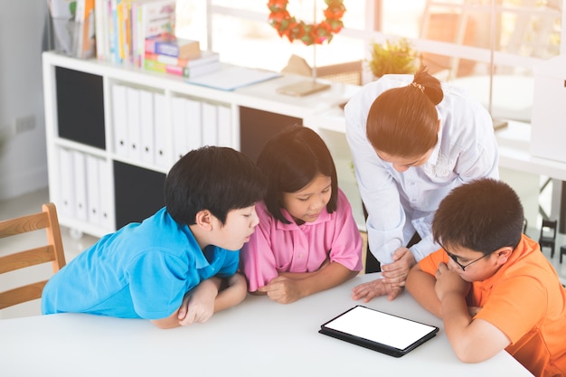 Insegnante e bambini asiatici che si divertono facendo uso della compressa digitale