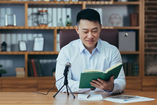 Asian teacher records online business course uses microphone records audio podcast and reads audiobook Businessman mentor works in university office