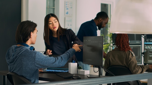 Asian team of IT engineers analyzing html code on terminal window, using server database on computer. Coders talking about programming language and cloud computing user interface.