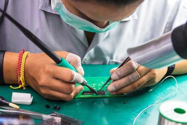 The asian technician repairing circuit board by soldering.