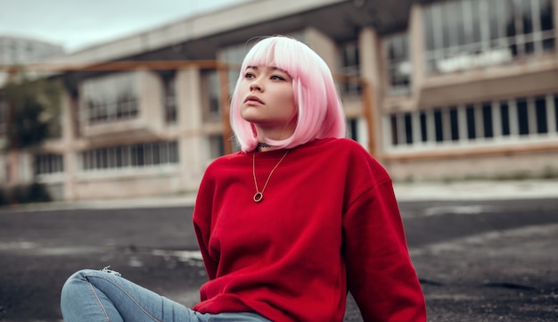 Asian teen girl looking away while sitting on ground in city