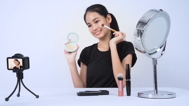 Asian teen woman sit in front of camera and live broadcasting as a beauty blogger influencer or youtuber to review or advice about how to make up at home. 