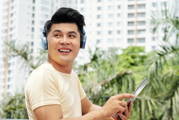 Asian teenage boy in headphones listening to music using his digital tablet outdoors