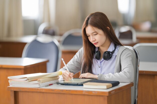 Asian teenage girl university student studying online via a digital tablet in the classroom