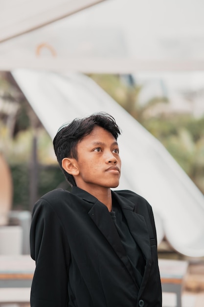 An Asian teenager in a black denim jacket leans against a garden table while relaxing and enjoying the view