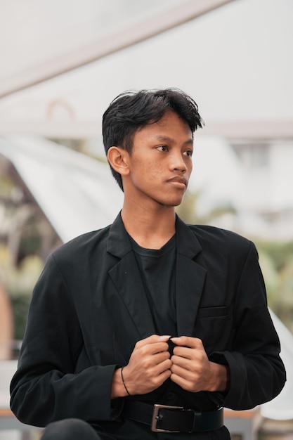 An Asian teenager in a black denim jacket leans against a garden table while relaxing and enjoying the view