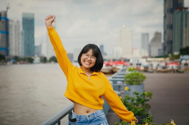 Felicità asiatica dell'adolescente che alza la mano contro l'orizzonte della città