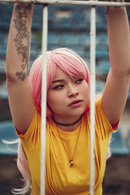 Азиатский подросток в розовом парике, опираясь на барьер