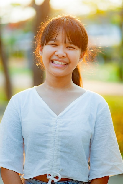 Asian teenager toothy smiling with happiness standing outdoor against beautiful evening light