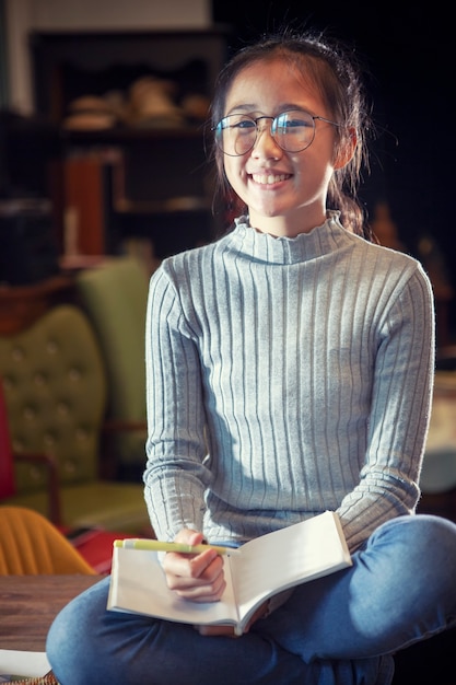 Asian teenager wearing eye glasses doing home work with stack of school book foreground