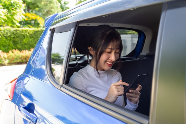 Donna asiatica dell'adolescente che utilizza uno smartphone nel sedile posteriore dell'automobile