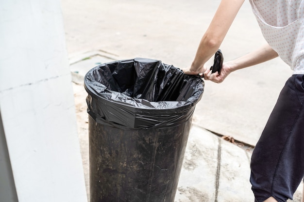 Photo asian thai housewife is prepare the garbage plastic black bag at the fron of her house.